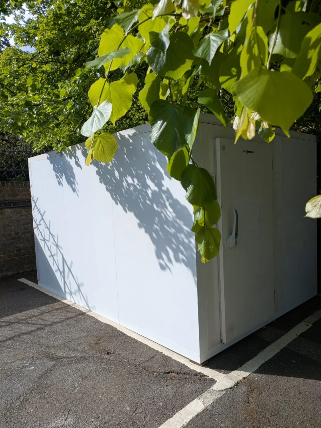 Side view of a VCS modular cold room installed outdoors beside a brick wall and trees